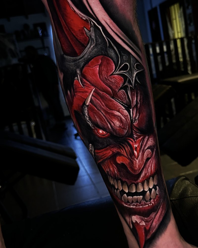 Buntes Oni-Masken-Tattoo in Rot und Schwarz am Schienbein, LSD Tattoo Berlin