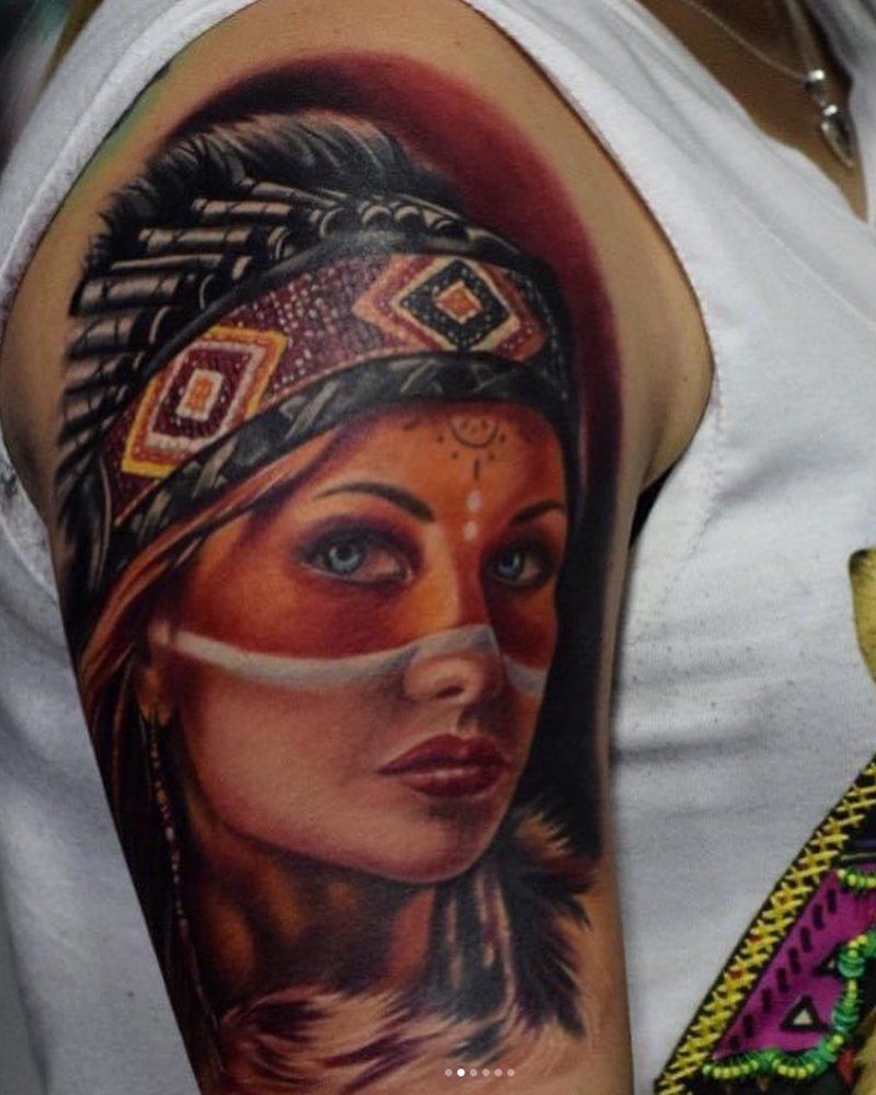 Farbiges Porträt-Tattoo einer Frau mit Federschmuck am Oberarm, LSD Tattoo Berlin